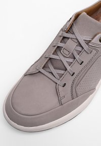 Baskets grises avec tige en cuir lisse, accents en mesh texturé, semelle en caoutchouc blanche et lacets plats. Présente des détails perforés sur les côtés.