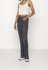 Haut blanc ajusté et court avec des bretelles nouées, associé à un jean évasé gris foncé et des baskets noires avec des accents blancs et une semelle marron.