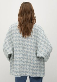 Jasnoniebieska, wzorzysta, oversize'owa kurtka z teksturowanej tkaniny o szerokich rękawach, z motywem pepitki na jaśniejszym tle.