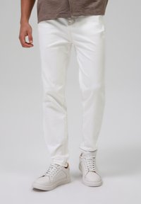 Jeans in denim bianco slim fit, con cuciture visibili e design a cinque tasche, abbinati a sneakers bianche basse.