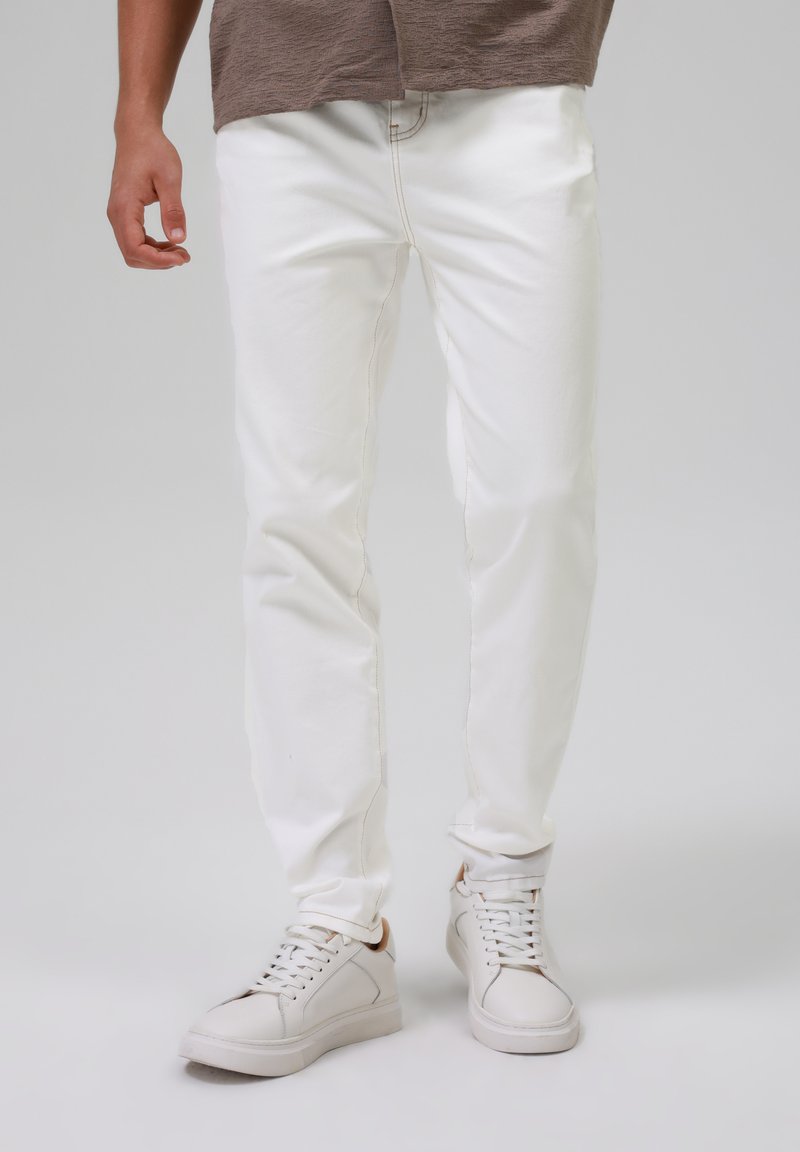 Jeans de mezclilla blanca con un corte ajustado, que cuentan con costuras visibles y un diseño de cinco bolsillos, combinados con zapatillas blancas de caña baja.