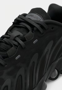 Baskets Nike Air Max noires avec lacets texturés, motifs latéraux ondulés et détail visible de la semelle à coussin d’air.