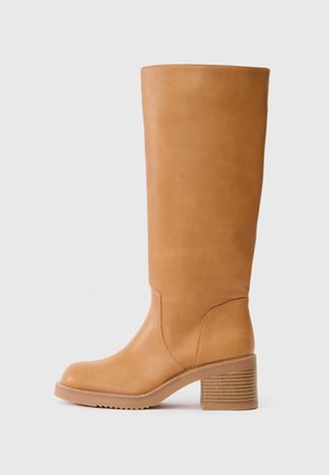Bota alta de couro castanho com bico arredondado, salto em bloco texturizado e acabamento suave. Apresenta costura discreta e um contorno limpo.
