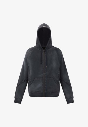 Zwarte zip-up hoodie gemaakt van zachte stof, met decoratieve studaccenten langs de naden en op de voorzakken. Gladde textuur.