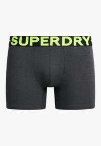 Pantalones cortos grises de tela con una textura suave, que presentan una cinturilla negra con el texto amarillo brillante "SUPERDRY".