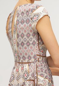 Robe à motifs avec un dos décolleté, des manches courtes type papillon, et une jupe évasée ; matériaux comprenant un tissu léger avec des dessins géométriques et floraux.