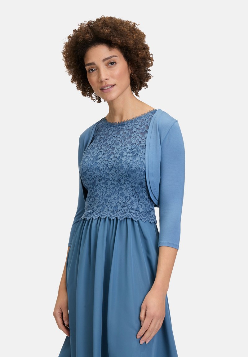 Lace top in zachte blauwe kleur met geschulpte randen, gecombineerd met een vloeiende rok. Lichtgewicht, lange mouwen en gestructureerde kant zorgen voor detail.