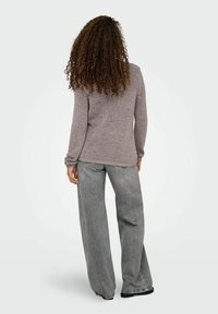 Pull en maille grise à manches longues et coupe décontractée, associé à un jean large gris clair. L'ensemble a une apparence décontractée et texturée.