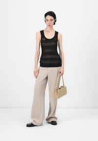 Svart strikket tanktopp med rund hals, kombinert med beige vide bukser og en lys beige veske. Svart flatsko fullfører antrekket.