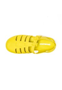 Sandalia de plástico amarilla con punta cerrada y talón abierto, que presenta un diseño de correas cruzadas y una hebilla ajustable única.