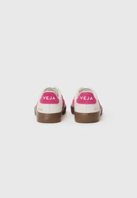 Hvite sneakers med rosa semsket skinn-detaljer, brune gummisåler, og VEJA-merke på hælen. Laget av bærekraftige materialer.