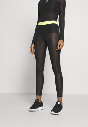 T-shirt de sport en mesh noir et leggings avec une taille en néon jaune, arborant des accents de logo et une coupe ajustée. Portés avec des baskets noires.
