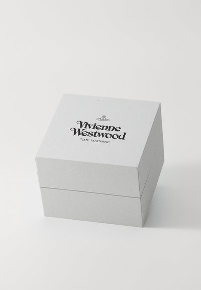Pelēks kartona kaitinājums ar salokāmu vāku, uz kura ir melns teksts "Vivienne Westwood TIME MACHINE" un neliela logo augšpusē.