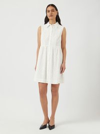 Rochie albă fără mâneci cu guler, prezentând modele tăiate intricate, închidere cu nasturi și fustă evazată. Pantofi negri cu vârf ascuțit.