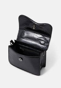Sac en cuir noir embossé crocodile, ouvert pour révéler un compartiment et une poche zippée. Il comporte un fermoir à pression et des accents en métal brillant.