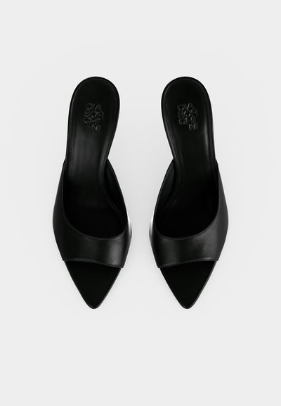 Ζευγάρι μαύρες δερμάτινες ανοιχτές γόβες χωρίς λουράκι, με μυτερά δάκτυλα, από πάνω σε απλό λευκό φόντο.