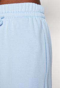 Ljusblå mjukisbyxor med elastisk midja och sidoficka, sydda av en person med en medelbrun hudton.