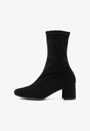 Stivali neri alla caviglia con una tomaia aderente simile a una calza, punta squadrata e tacco a blocco. Realizzati in tessuto morbido con dettagli di cucitura visibili.