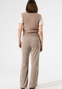 Beige gestrickte Weste mit geripptem Saum, kombiniert mit hellbraunen Kordhosen, die eine weiche Textur und Gesäßtaschen aufweisen.
