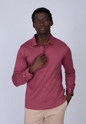 Polo à manches longues en rose poussiéreux, fabriqué en tissu doux, avec un col, une patte de boutonnage à deux boutons et un branding subtil sur la poitrine.