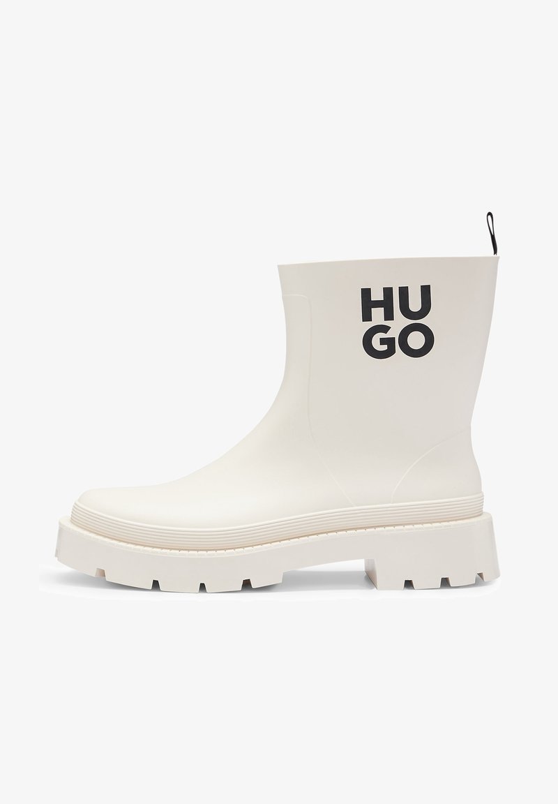 Witte rubberen enkelboot met een chunky zool, zijbranding "HU GO," textuurdetails op de bovenkant en een aantreklus aan de achterkant.