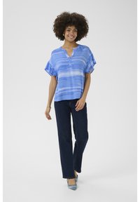 Zila rakstota īsām piedurknēm blūze ar V veida kakla izgriezumu, apvienota ar tumši ziliem džinsiem un gaiši ziliem apaviem; gluda auduma un brīvs pielietojums.