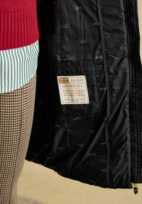 Czarna pikowana kurtka z podszewką w małe zielone wzory królików. Zawiera metkę z napisem "JOULES", która informuje o trwałości od "miasta po wieś".