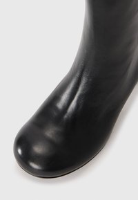 Black leather ankle boot with a smooth, glossy texture and rounded toe, featuring a fitted shaft that contours closely to the foot.