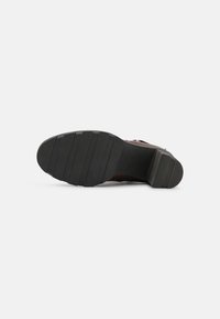Chaussure en cuir marron avec une semelle en caoutchouc noir solide. Présente des rainures horizontales pour l'adhérence et un talon carré pour la stabilité.