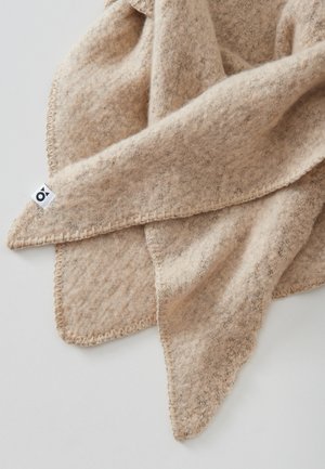 Beige Wolledecke mit strukturierter Oberfläche, mit einem gestickten Rand und einem kleinen Etikett in einer Ecke. Weicher und gemütlicher Eindruck.