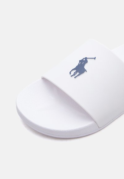 Λευκό σανδάλι με σαγρέ πάτο και λογότυπο ποδοσφαιριστή πόλο σε σκούρο μπλε χρώμα στο φαρδύ λουράκι πάνω από το πόδι.