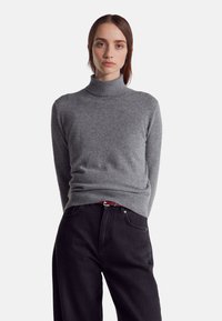 Šedý rolák vyrobený z měkké pleteniny, s přiléhavým střihem. V kombinaci s černými džíny s vysokým pasem a kontrastním pásem.