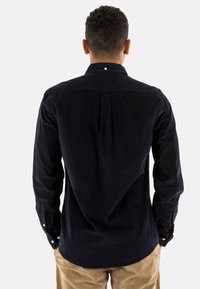 Navy corduroy overhemd met een button-down kraag, lange mouwen, schouderpas en rugplooien. Voorzien van witte knopen op de manchetten.
