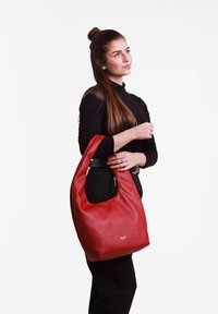 Red leather shoulder bag with a curved shape and visible zipper detail. Features a smooth texture and a small logo on the front.