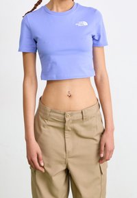 Croptop en coton lavande clair avec des manches courtes et un col rond ; présente un logo blanc sur la poitrine gauche. Assorti à un pantalon cargo beige.