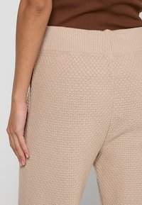 Beige knitted leggings featuring a textured pattern, a wide ribbed waistband, and a form-fitting design for comfort and flexibility.