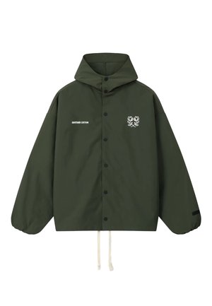 Mørkegrøn hættejakke med trykknapper foran, hvide snore, hvid tekst "ANOTHER COTTON" og et grafisk motiv af en bomuldsplante på forsiden.