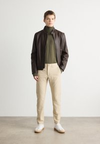 Brown leather jacket with a high collar, olive green turtleneck, beige trousers, and white sneakers with gum soles. Minimalistic design.