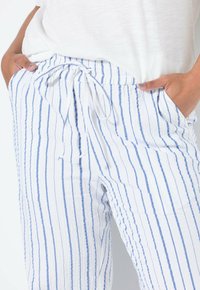 Leichte, gestreifte Hose in Weiß mit blauen vertikalen Linien. Verfügt über einen Kordelzugbund und Seitentaschen. Weiches, strukturiertes Gewebe.
