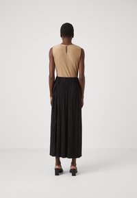 Vestido sin mangas con un top plisado beige y una falda plisada negra. Detalle de espalda con abertura y cinturilla elástica. Sandalias negras de tacón cuadrado.