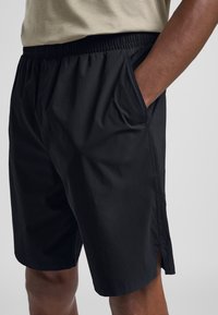 Pantaloni corti neri con una vita elastica, tasche laterali e un tessuto leggero e testurizzato. Presenta aperture laterali per facilitare i movimenti.