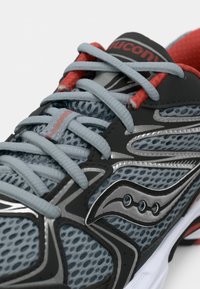 Ténis de corrida com um cabedal em malha cinza, detalhes prateados, sobreposições pretas e atacadores vermelhos; apresenta um design texturizado e respirável, além de uma sola acolchoada.