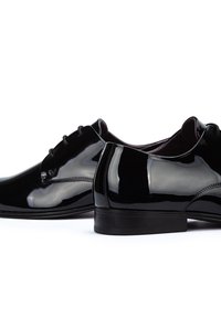 Zapatos de vestir de charol negro con un acabado suave y brillante. Cuentan con cordones, puntera redonda y un tacón bajo y sólido.