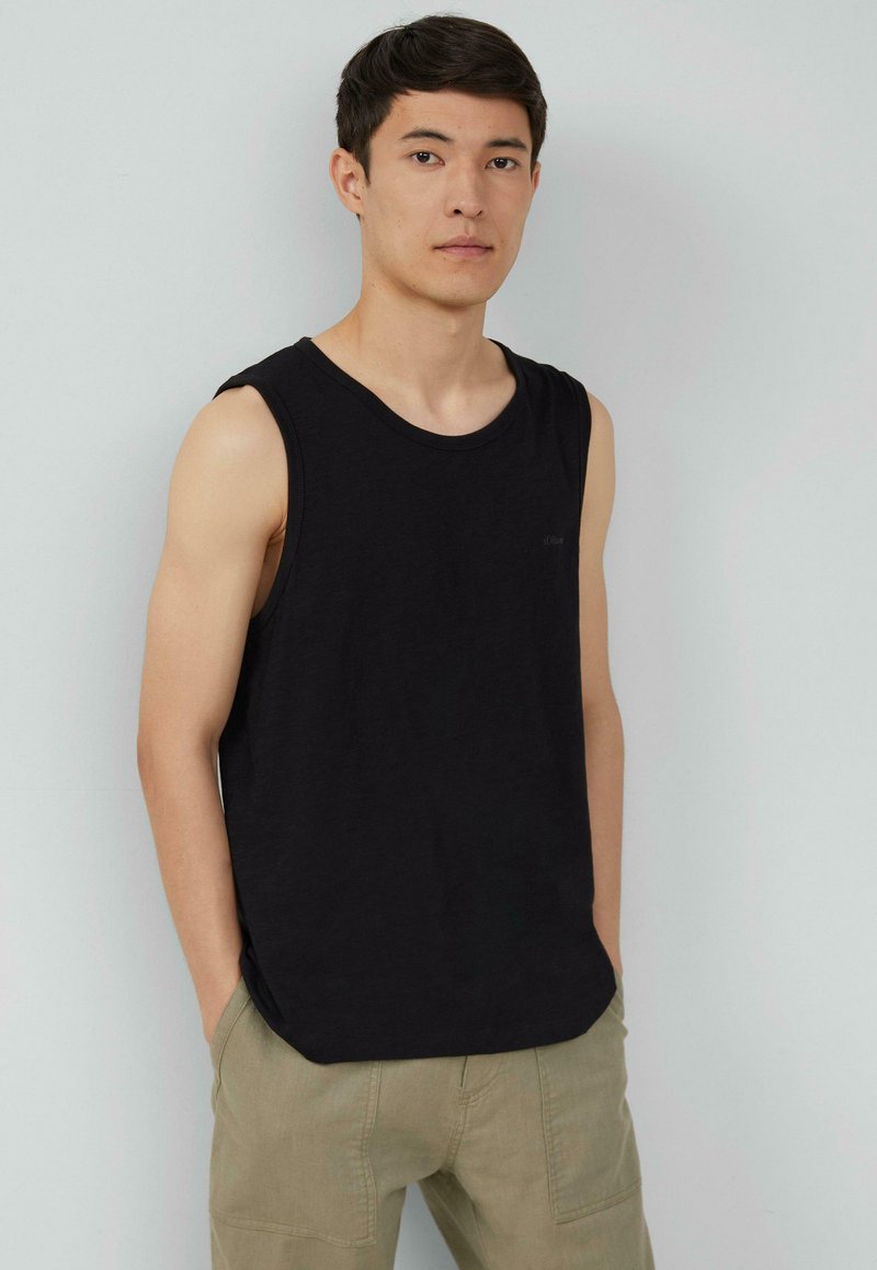 Zwarte mouwloze katoenen tanktop met een ronde halslijn, gedragen met lichtbeige cargobroek. Gladde textuur en minimale details.