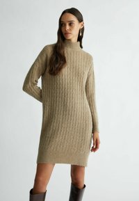 Abito in maglia marrone chiaro, con collo alto, texture a coste e dettaglio del logo sull'orlo, dotato di maniche lunghe.