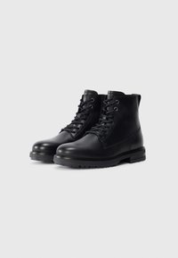 Black leather ankle boots with round toes, lace-up front, stitched details, and textured rubber soles for traction.