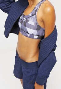 Conjunto atlético que presenta un sujetador deportivo gris con un patrón geométrico y una chaqueta texturizada azul marino, combinada con pantalones cortos azules marinos a juego.