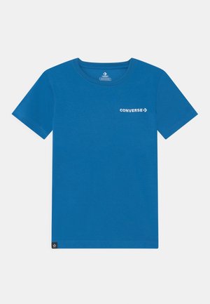 Niebieski t-shirt z krótkim rękawem z białym logo "Converse" na lewej piersi oraz małą czarną metką u dołu.