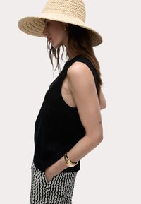 Top negro sin mangas combinado con pantalones de patrón en blanco y negro. La modelo lleva un sombrero de paja de ala ancha y una pulsera de oro.