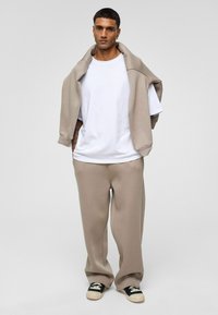 Beige sweatshirt over een wit T-shirt en bijpassende beige broek. Zwarte en witte sneakers maken de outfit compleet. Glad textuur van de stof.